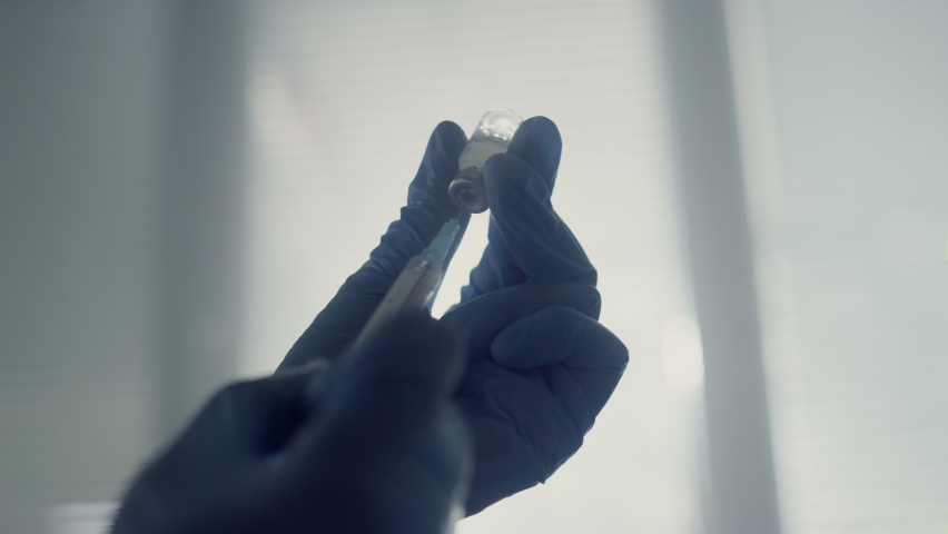 Unknown physician hands filling syringe with medication holding vial close up. Doctor preparing vaccine injection in modern clinic office wearing safety gloves. Coronavirus immunization concept. Royalty-Free Stock Footage #1090044687