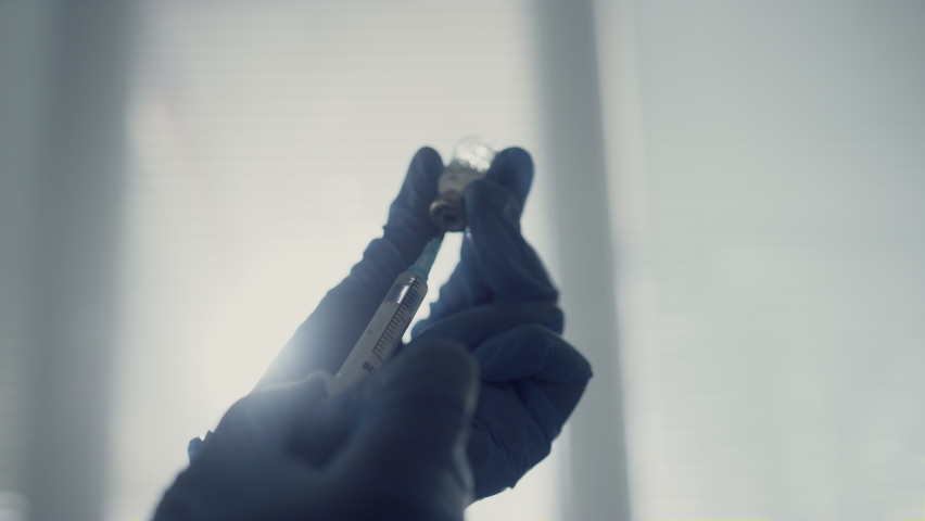 Unknown physician hands filling syringe with medication holding vial close up. Doctor preparing vaccine injection in modern clinic office wearing safety gloves. Coronavirus immunization concept. | Shutterstock HD Video #1090044687