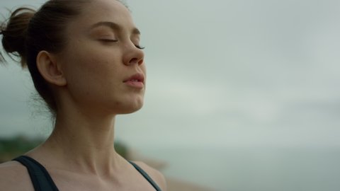 Yogi woman making deep breath meditating on beach cloudy morning close up. Sporty attractive girl doing relaxing exercise on nature. Portrait of european lady practicing yoga outdoor. Sport concept.