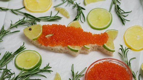 Sandwich with red caviar in shape of fish with lemon, rosemary rotate. Expensive healthy food concept on white background. Sandwiches bread toast with salmon caviar salted roe rotating slow motion
