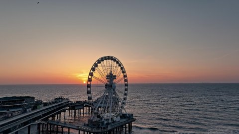 Drone shot around the Ferris wheel at the beach in Scheveningen, The Hague, Netherlands - including the pier and bungee jump. Takes place during sunset.