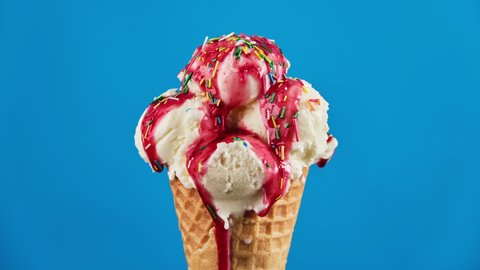 Timelapse of vanilla ice cream with strawberry topping and colorful sprinkles in waffle cone melting on blue background. Delicious white ice cream melting. Close-up of sweet dessert. Food concept