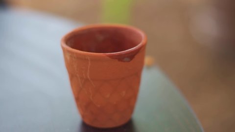 Closeup shot of hand of an Indian man picking up Tea in traditional clay cup also known as Kulhad at India. Man takes chai break and lifts tea from his table. 