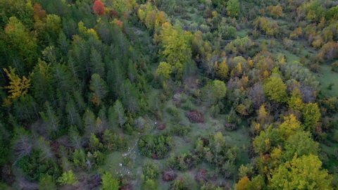 Aerial view of colorful fall foliage in middle of mountains in sunny Abruzzo, Italy - reverse, tilt, drone shot