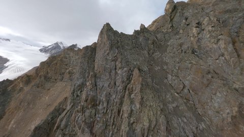FPV sports drone shot volcanic canyon valley scenery wilderness ridge panorama. Aerial view flying over organic mountain summit cracked texture stone pebble cliff geology formation surrounded by snow