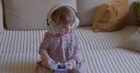 Cute little girl sits with headphones on her head, listens to sounds, smiles. Child exposed to maximum safe noise level of about 80-90 decibels to avoid hearing damage. Baby hearing.