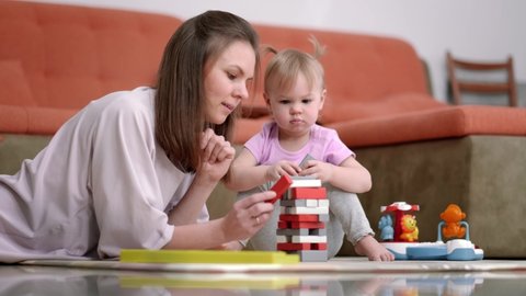 Little baby girl and mommy playing color wooden toys at home sitting on floor, Mother and daughter laughing having fun together