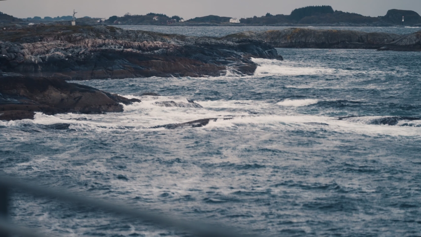 Powerful waves are crashing on the rocky shores near the Atlantic road, in Norway. Seagulls fly low above the water. Slow-motion, pan left.