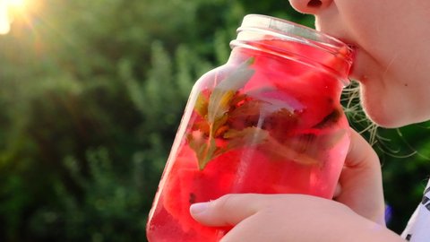 watermelon drink with stevia.little girl drinks a watermelon drink from a mug in a summer garden. child drinks a red cold cocktail from a glass misted mug.Watermelon diet smoothie. High quality 4k