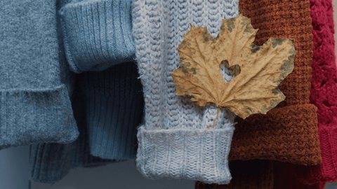 Autumn concept. Female hand put maple leaf in heart shape on cozy warm sweater. Knitted woolen and mohair sweaters. Hygge style