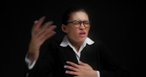 Business lady with glasses suffers from chest pain at work. A beautiful Asian woman in office clothes has a heartache, a heart attack, myocarditis, she has fever, pressure. On a black background