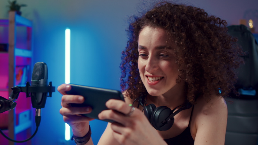 Happy woman girl gamer wear headphone competition play video game online with smartphone colorful neon lights in living room at home. Esport streaming game online, Home quarantine activity concept. | Shutterstock HD Video #1090069131