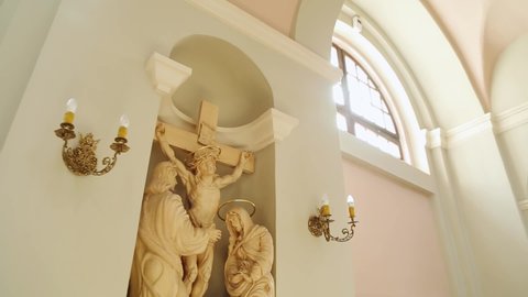 Minsk, Belarus - July 15 2014: Sculpture of crucifixion of Jesus Christ in crown of thorns in niche of interior church. Sunbeam falls on biblical composition from windows, camera moves around object.