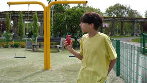 WROCLAW, POLAND - MAY 06, 2022: Teenager boy kid drinking coca cola can standing on playground for children outdoors