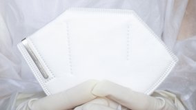 4 k doctor nurse or medical assistant in white gloves and disposable robe is removing or holding in hand a respiratory protection mask FFP2. viruses protection. close up video