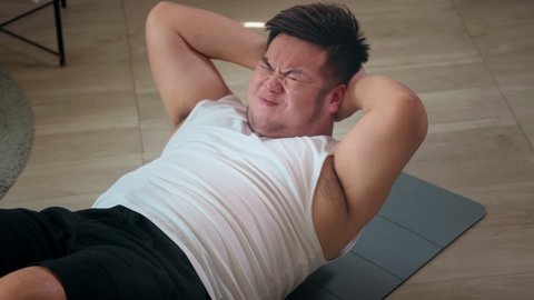 Close-up of a chubby man endeavor to do sit-up at home for weight loss and burning fat calories training. Asian male people Plus size in sportswear workout for good body and healthy