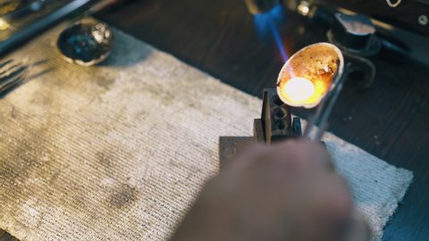 CU: skilled jeweler pours molten metal into form from small crucible at table with asbestos cover in workshop closeup
