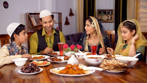 A cheerful Muslim family eating together during the festive season - the dinner table, Eid celebrations, family time. Happy Indian family - A young father, Indian mother and kids, family bonding.