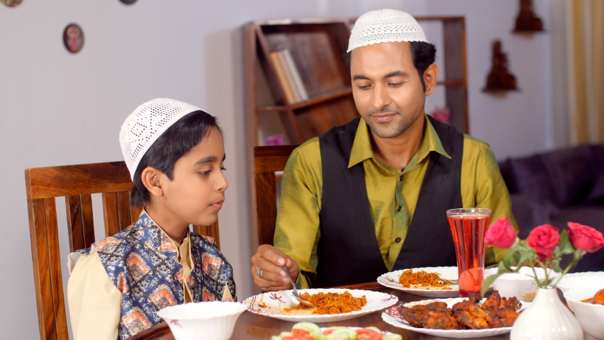 A Muslim man and his little kid in ethnic wear during the festive season - family bonding, leisure time, white skull cap, culture . A happy father feeding his son - happy parenting, love and care. Royalty-Free Stock Footage #1090074865