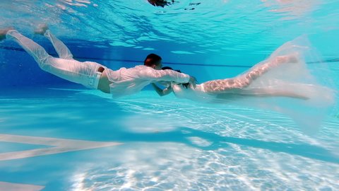 Brides in wedding dresses swim in the pool underwater. beautiful newlywed couple. The water is clear and blue. In love