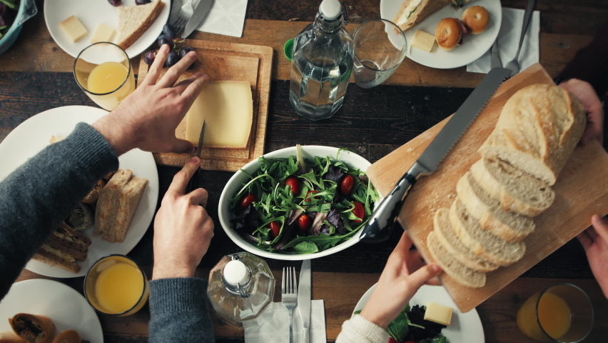 A group of friends having lunch together at a table from above. Friends at a party reaching for food on the table at brunch from above. A group of friends celebrating and eating a meal together Royalty-Free Stock Footage #1090076633