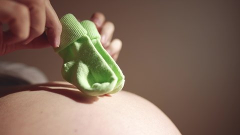 happy pregnant woman. booties baby shoes on the belly of a pregnant woman. pregnancy health procreation concept. close-up belly of a pregnant woman. woman waiting for a newborn indoor baby