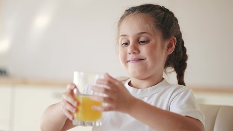 girl child drinking juice. happy family a healthy eating kid dream concept. indoors daughter girl drinking yellow juice from a glass cup in the kitchen. child drinking fruit juice