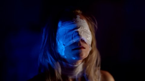 portrait of blindfolded woman in darkness, lady with bandages on eyes is standing alone in dark room