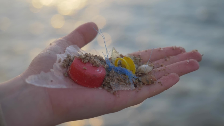 Environmental pollution problem - plastic waste in hand, sea shore on the background. disposable or single use plastic, microplastics. Beach sand and ocean pollution. | Shutterstock HD Video #1090077199