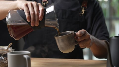 Barista pouring steaming drip coffee with smoke in to a cup on a work desk in coffee shop
