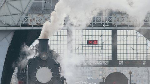 Steam locomotive train approaching station passing through goods yard leaking smoke and steam ignited from behind, creating an atmospheric.