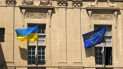 The Ukraine flag and European flag at the window waving in the wind. In support of the invasion of the Ukraine and its joining the European Union. Europeans support Ukraine joining the EU.