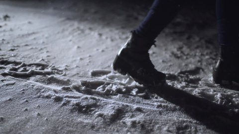 Close-up of female legs steps in winter snowy dark park. Woman walking in winter night. Black winter boots on legs. Snow falling in darkness. Female In Snowy Weather At Cold Temperature Running Alone
