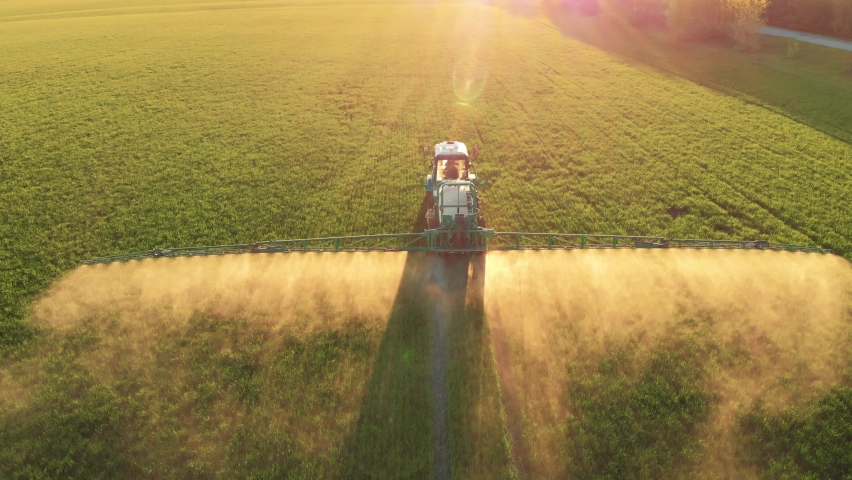 Aerial footage. Pesticide Sprayer Tractor working on a large green field at sunset. Aerial shot following on the side a tractor spraying wheat field against diseases. Farmer spraying soybean fields. Royalty-Free Stock Footage #1090079571