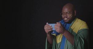 Afro american man, wearing Brazilian clothes, football fan, watching the game on mobile, technology, online, connected. World Cup, Olympics. 4K Premium Cinematic Video.