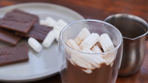 Stir with a spoon marshmallow in a glass of milk cocoa. Nutritious chocolate drink with cookies. Great snack. Slow motion, close-up