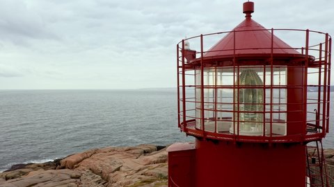 Lens prism with rotating glass around bulb inside Ryvingen lighthopuse Norway - Static closeup aerial showing top of red lighthouse with north sea background