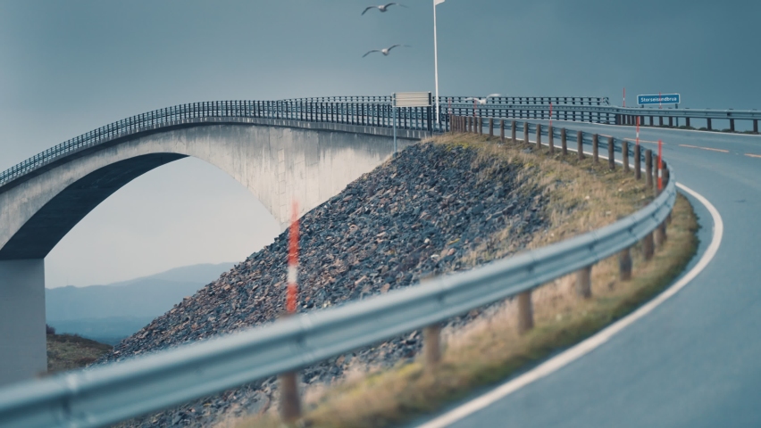 Storseisundet bridge on the Atlantic road spanning above the turbulent waters. Seagulls fly low above the road. Slow-motion, pan forward.