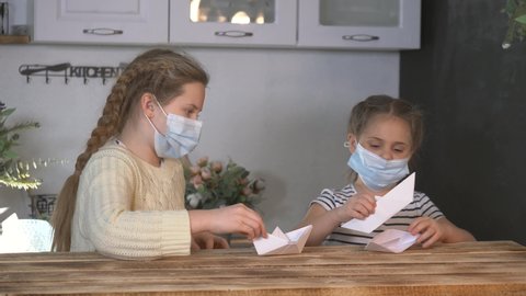 Children in isolation sit at home in a medical mask. Children play and learn at home with the help of computer technology. Homeschooling in isolation during a pandemic. Children in medical masks play.
