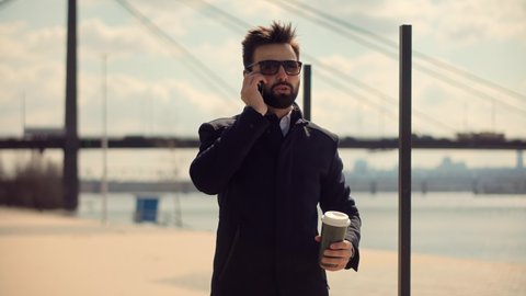 Young Attractive Bearded Man Sitting And Talking On Mobile Phone With Friend.Businessman Using Mobile Phone At Beautiful Place.Handsome Bearded Man Talking By Smartphone.Man Talking On Mobile Phone.