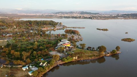 Aerial Circling Over Park And Shoreline Around Rawal Lake Shore With The City In The Background - Islamabad, Pakistan