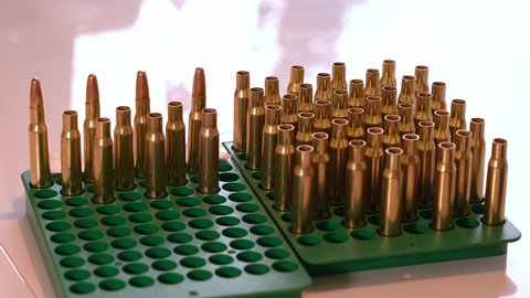 Hand picking up empty brass rifle casings from tray to add gunpowder - Static closeup of tray with both empty casings and ready ammunition with bullet