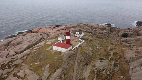 Approaching Ryvingen lighthouse in eliptical pattern with atlantic ocean in background - Traditional lighthouse tower on island on Norway southern coastline outside Mandal - Aerial