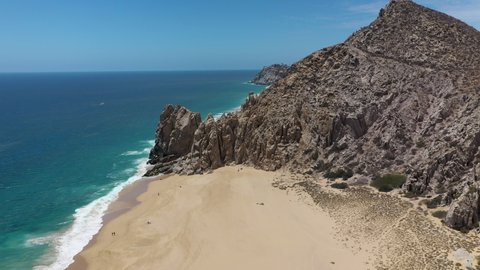 Drone shot of sea cliffs and beaches, revealing resorts on Playa El Médano in Cabo San Lucas Mexico, wide and rotating