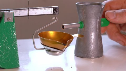 Person turning powder trickler to add last drops of gunpowder to mechanic weight scale - Home ammunition reloading process static closeup