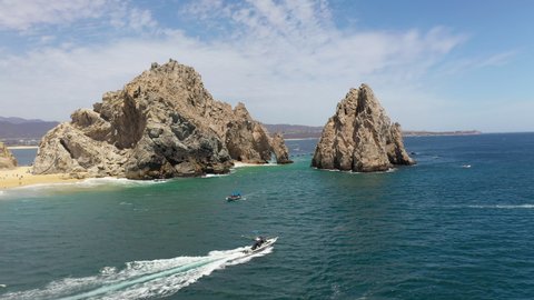 Wide drone shot of boats in the ocean with sea cliffs in the background in Cabo San Lucas Mexico, rotating