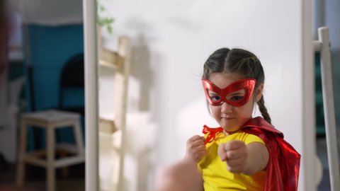 Girl in superhero mask. Child in hero costume. Happy child is winner. Girl is playing at home.Kid in front of mirror in hero mask.Girl play in superhero costume.Successful child with smile on his face