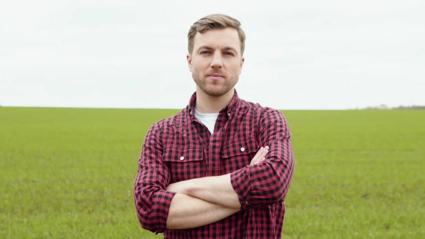 Portrait shot of attractive farmer standing in green field, smiling cheerfully to camera. Farmer with smile outdoors in summer