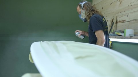 Surfboard manufacturing, Shaper paints a surfboard. Concept of surfing industry production, modern active lifestyle, skilled professional, millennial worker in America. 