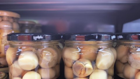 Marinated champignons in glass jars stand on a supermarket shelf. Closeup